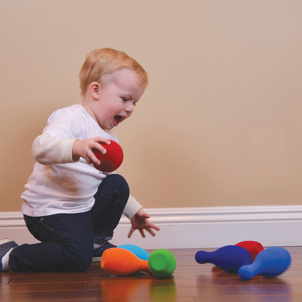 Little boy striking down the pins in the 7 piece Bowling Set that has 6 colorful pins and 1 red bowling ball.