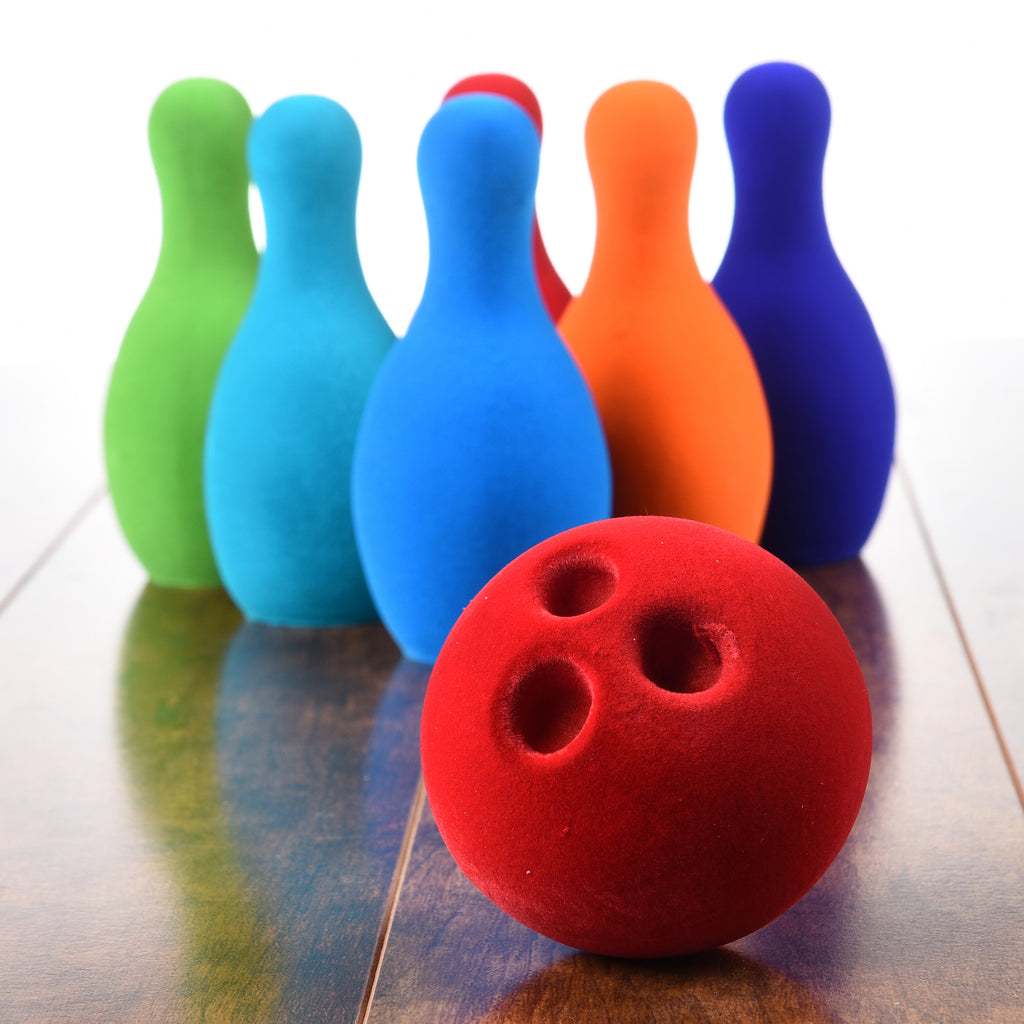 Bowling set with red bowling ball and six colorful pins on floor of a house.