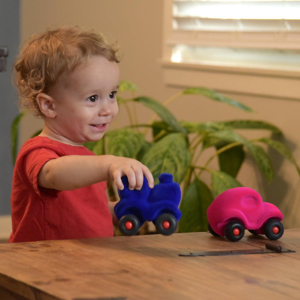 Boy playing with Rubbabu® vehicle toys, including the pink car from the Set of 8 Little Vehicle Assortment. 